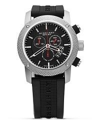 A cool and current look from Burberry Sport. The three eye chronograph has a round dial in black with white and red accents. Textured bezel and black rubber strap. A cool and current look from Burberry Sport. The three eye chronograph has a round dial in black with white and red accents. Textured bezel and black rubber strap.