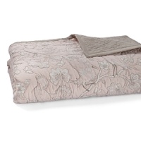 A delicately stitched quilt, printed with floral branches and birds in muted hues of tan and pink. A delicately stitched quilt, printed with floral branches and birds in muted hues of tan and pink.