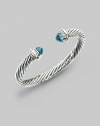 From the Silver Classics Collection. The signature Yurman cable bangle, capped with faceted blue topaz domes and accents of 14k gold. Blue topaz Sterling silver and 14k yellow gold Cable, 7mm Diameter, about 2¼ Imported