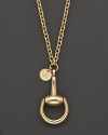 A bold horsebit pendant and a logo tag dangle from a gleaming 18K yellow gold chain.