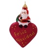 A little Santa sits atop a glittered puffed heart to wish you a Feliz Navidad.