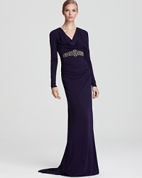 A jeweled waistband lends brilliance to a standout cowl neck gown from Badgley Mischka, rendered in a royal purple hue. A jeweled waistband lends brilliance to a standout cowl neck gown from Badgley Mischka, rendered in a royal purple hue.