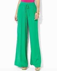 A breezy wide-leg pant is crafted with a soft, sueded crepe construction featuring a comfortable smocked waistband for ease and style. A breezy wide-leg pant is crafted with a soft, sueded crepe construction featuring a comfortable smocked waistband for ease and style.